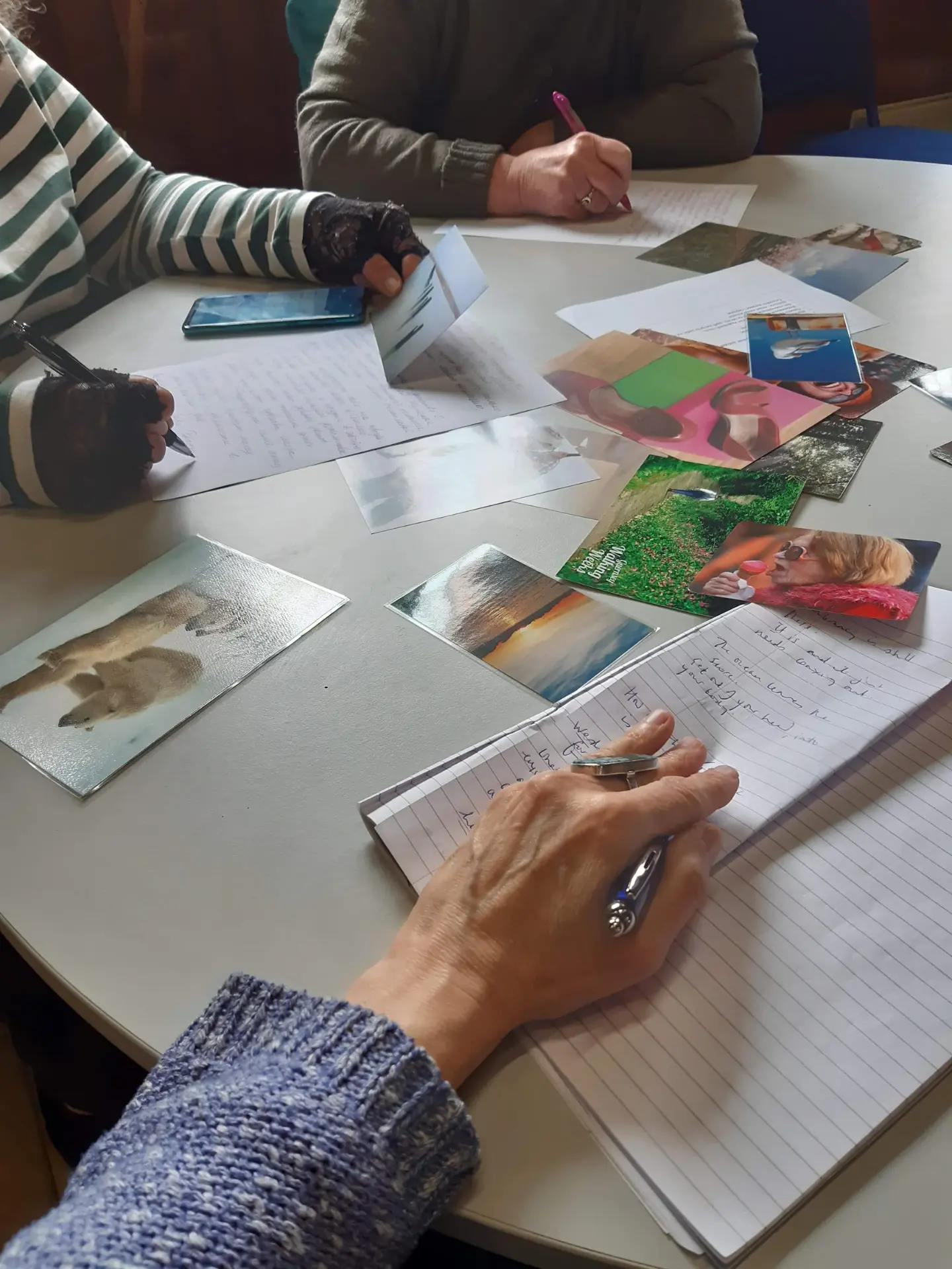 Participants writing at a table scattered with photographs and papers