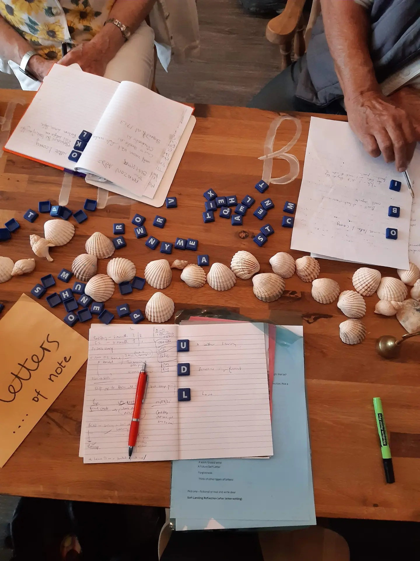 Shells, letter tiles and handwritten notes spread across a wooden table
